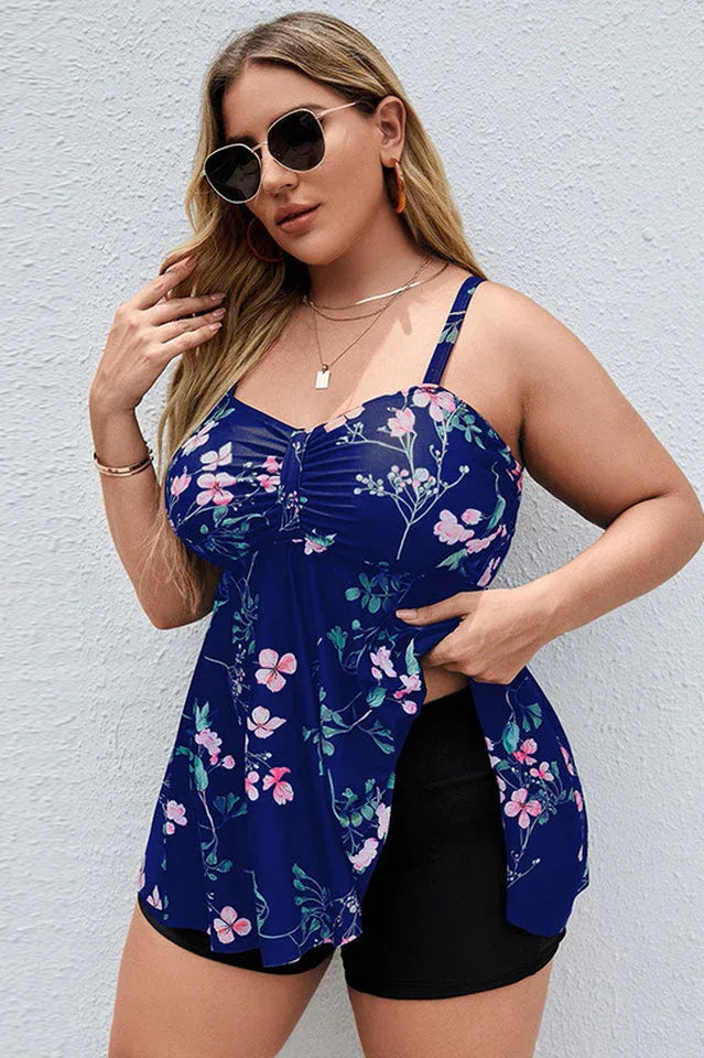 Plus-size woman wearing a navy blue floral print tankini with black shorts, against a light-colored wall.