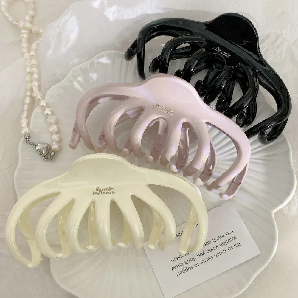 overhead view of three octopus claw hair clips in black, pink, and cream with pearls