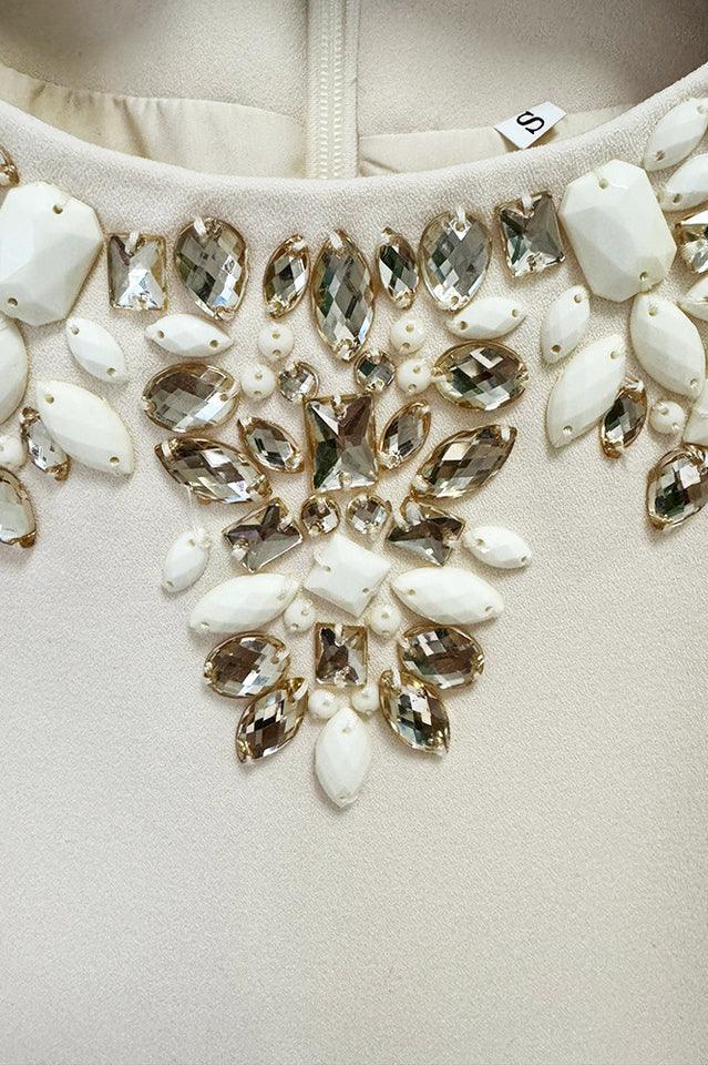 Detailed view of the embellished neckline of a cream-colored dress, showcasing a cluster of clear and opaque white stones.