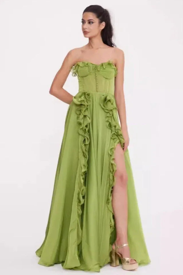 Woman in a green strapless satin gown with ruffled detailing and a high slit, side view.