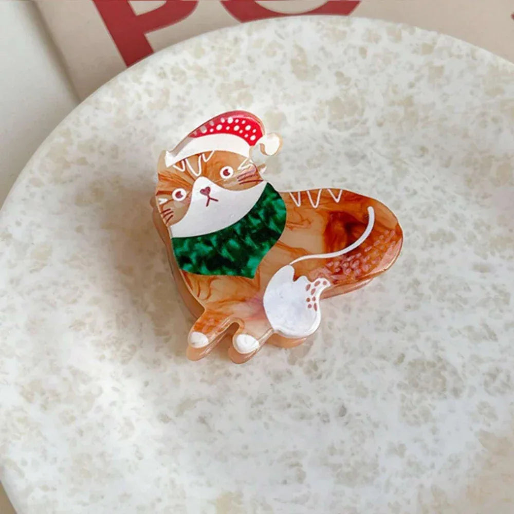 Orange and white tabby cat brooch with a festive scarf and hat, placed on a white surface.