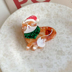 Orange and white tabby cat brooch with a festive scarf and hat, placed on a white surface.