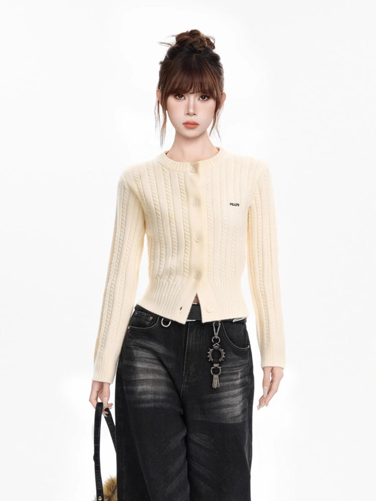 Woman wearing a cream cable knit cropped cardigan with black jeans and a black belt, holding a black fur bag
