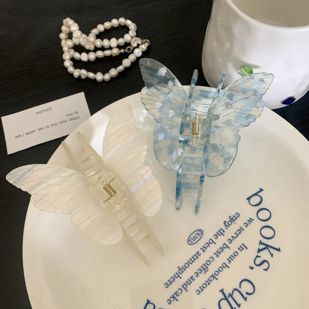 Two butterfly-shaped hair claw clips, one white and one blue with white marbling, displayed on a white plate with blue text.