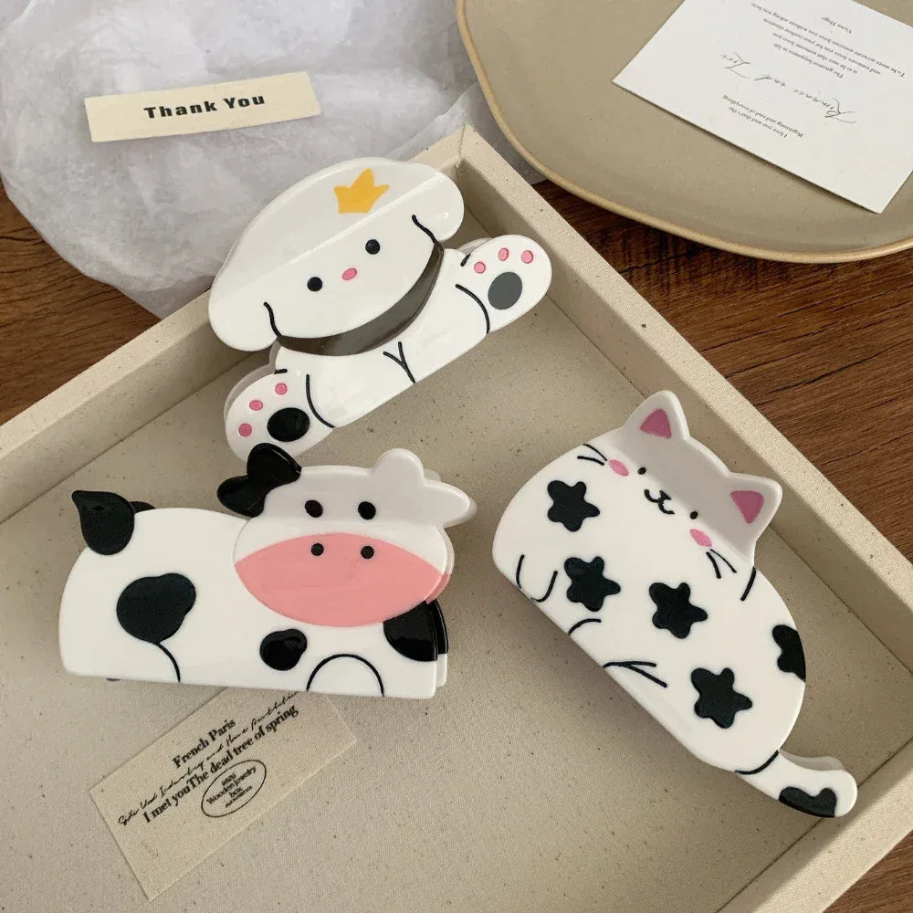 A collection of three animal-shaped hair clips, including a cow, a dog, and a cat, arranged in a tray.