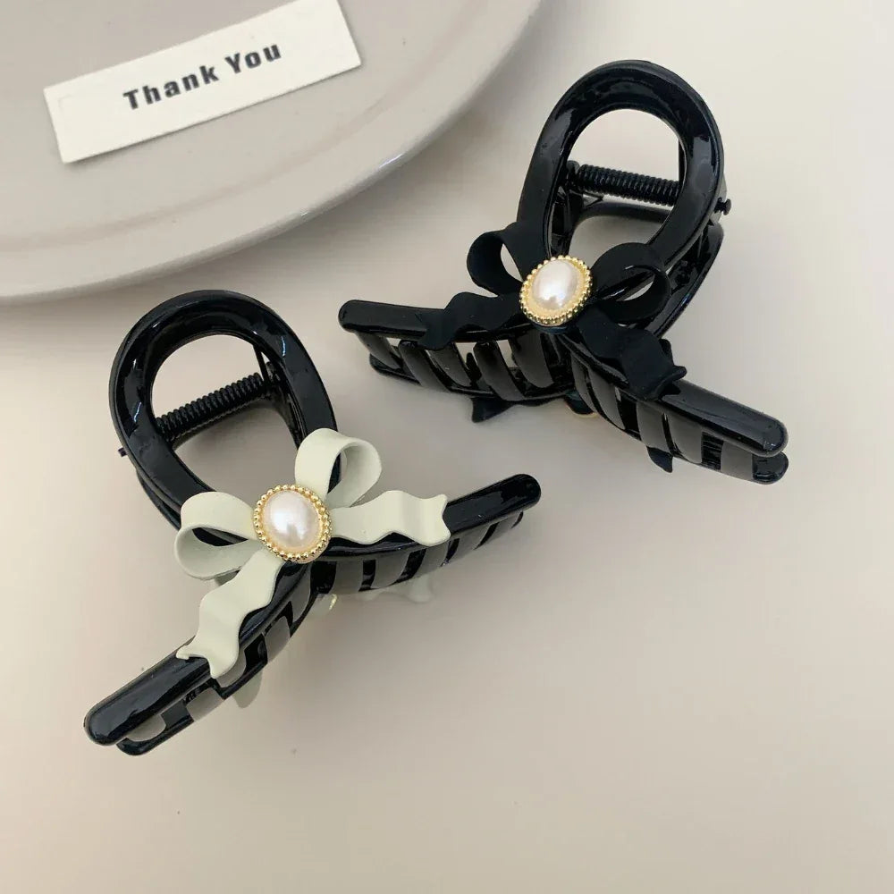 Two black hair claw clips with pearl accents, one with a black bow and one with a light green bow, on a plate