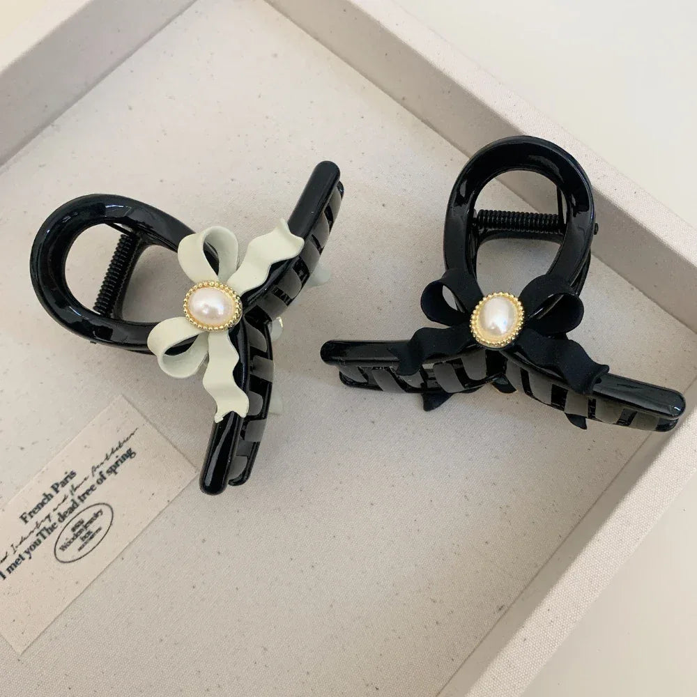 Two black hair claw clips with pearl accents and bows, displayed on a tray