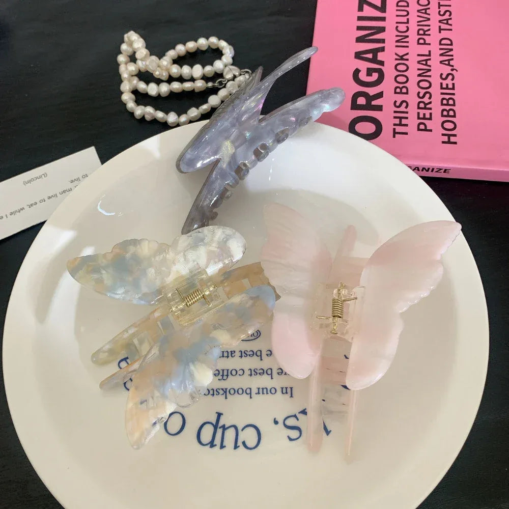 A selection of butterfly-shaped hair claw clips in pastel colors, including purple, pink, and marbled blue and white, displayed on a white plate.