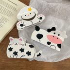 A variety of cute animal hair clips, including a cow, a dog, and a cat, are arranged on a white surface next to an open book.