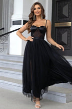 Woman in a black tulle maxi dress with a sweetheart neckline and high slit, standing on stairs.