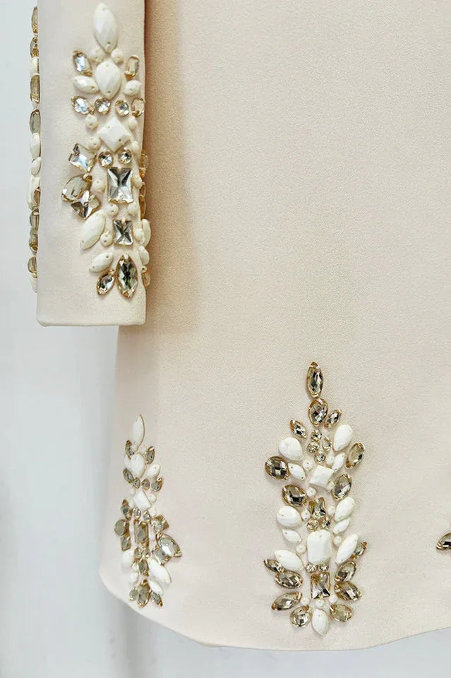 Detail shot of the embellished cuffs and hemline of a cream-colored dress, highlighting the sparkling crystal and pearl accents.
