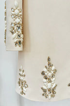 Detail shot of the embellished cuffs and hemline of a cream-colored dress, highlighting the sparkling crystal and pearl accents.