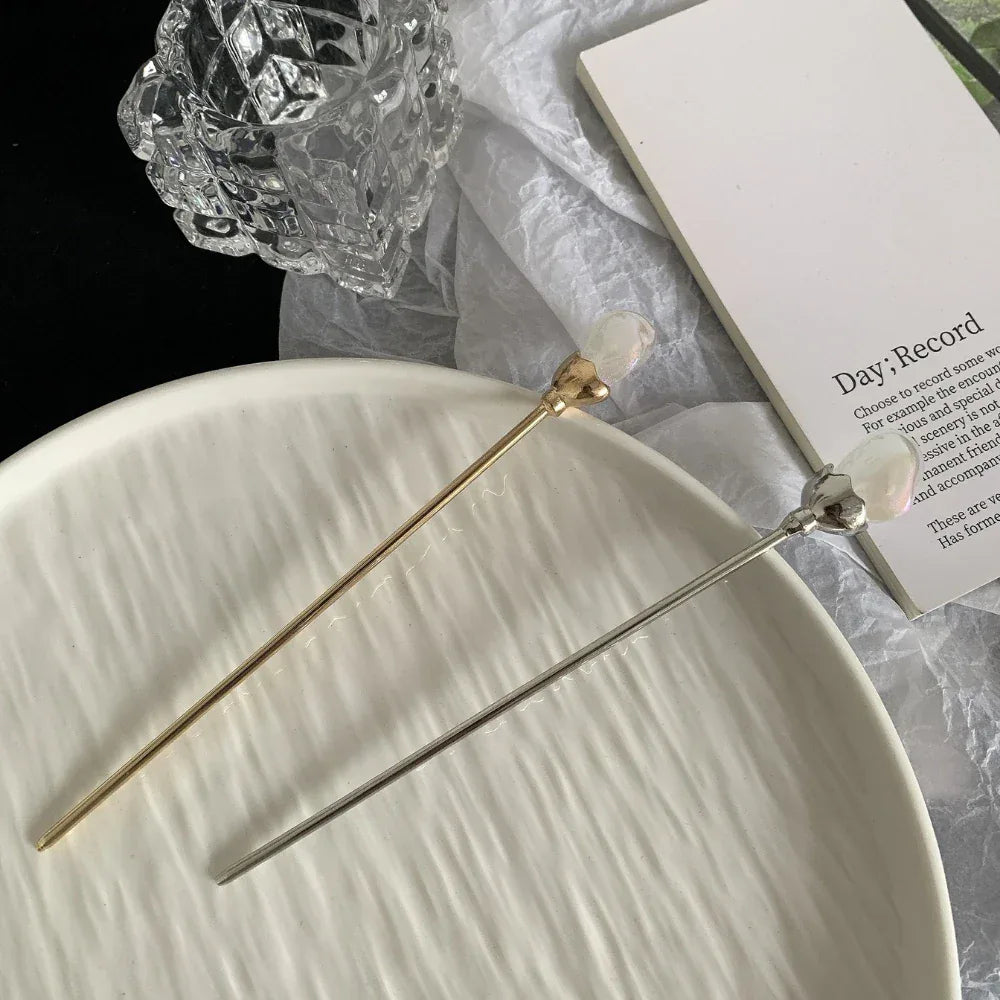A gold-tone and silver-tone hairpin are displayed on a white ceramic plate.