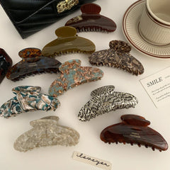 An assortment of tortoiseshell patterned hair claw clips scattered on a white surface, showcasing different colors and patterns, with a coffee cup and a note that says 'iloveyou'.