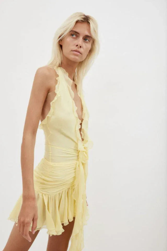 Side view of a woman wearing a yellow ruffled halter mini dress