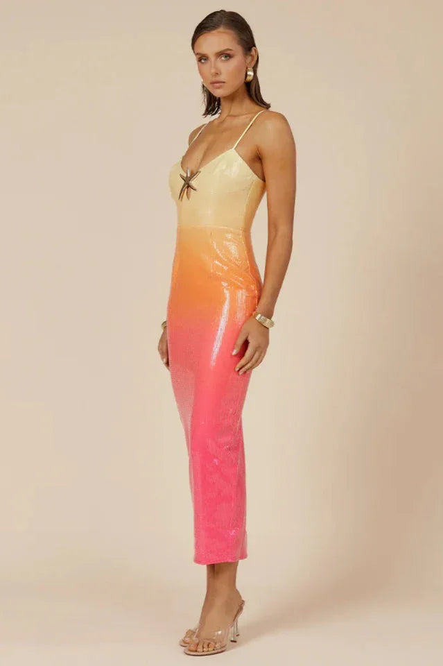 Side profile of a model wearing a yellow, orange, and pink ombre sequined midi dress with spaghetti straps and a star embellishment at the bust, against a neutral background.