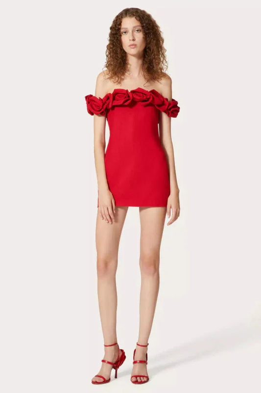 Woman wearing a red off-the-shoulder mini dress with rose embellishments on the neckline and red strappy heels.
