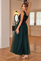 Woman in a floor-length dark green sequined and tulle formal dress with a v-neckline, shown from the back.