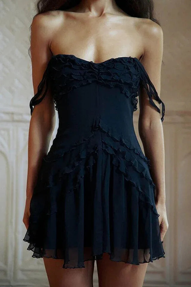 Close-up of a model wearing a black strapless mini dress with ruffle trim and sheer tiered skirt, front view.