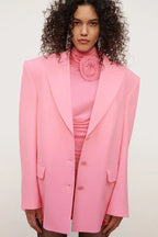 Model wearing a pink ruched mini dress with a mock neck and floral applique, styled with a pink blazer