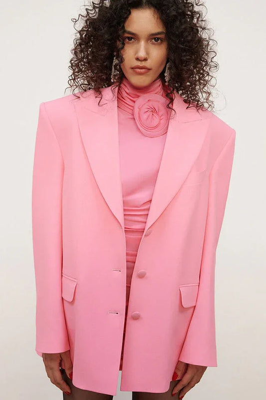 Model wearing a pink ruched mini dress with a mock neck and floral applique, styled with a pink blazer
