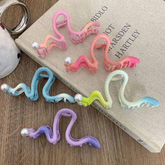 Collection of colorful S-shaped hair claw clips with pearls arranged on a book and saucer