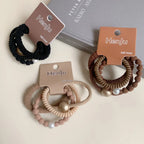 Three packaged sets of coiled hair ties, showcasing black, brown, and beige colorways with embellishments.