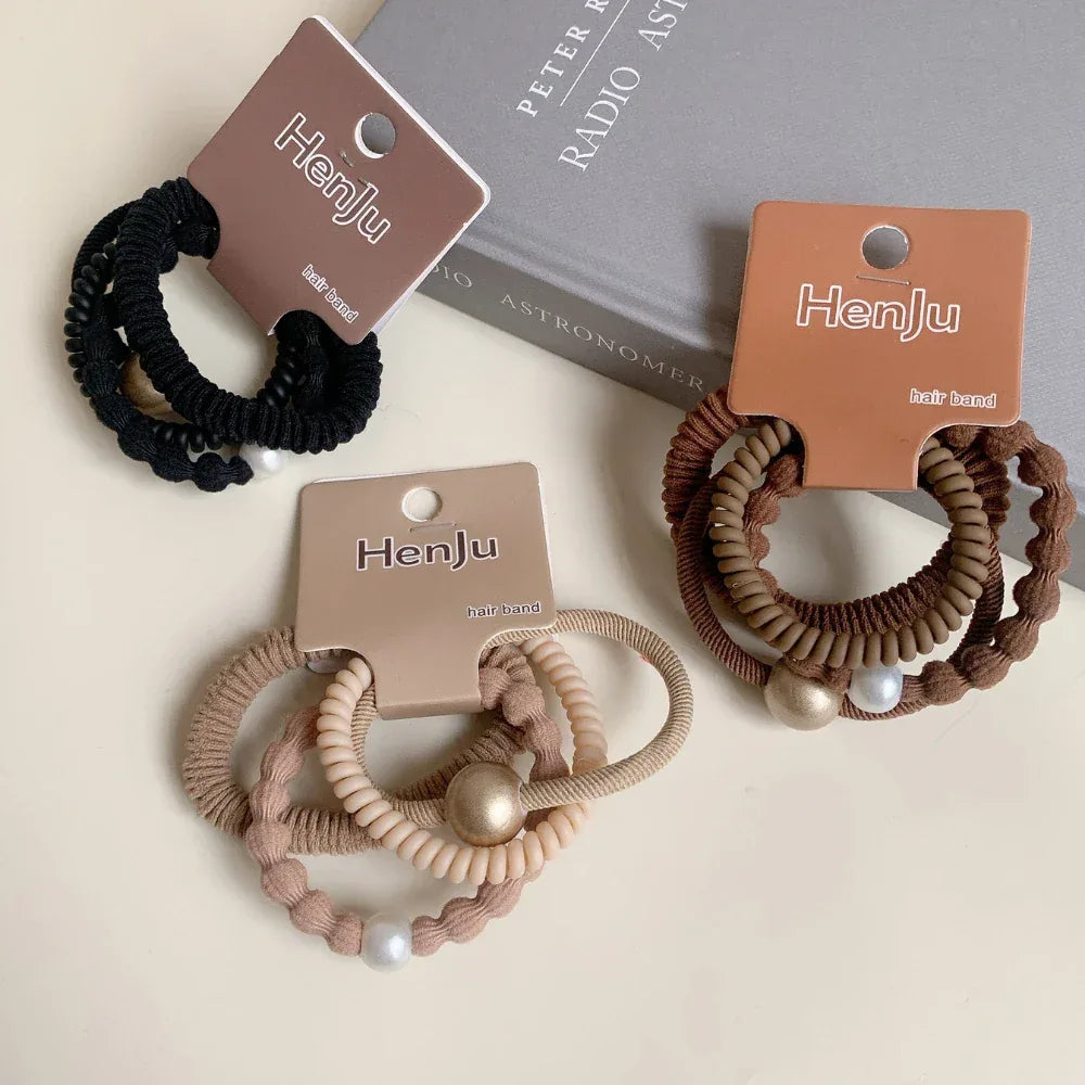 Three packaged sets of coiled hair ties, showcasing black, brown, and beige colorways with embellishments.