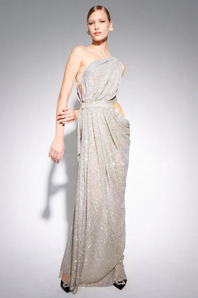 Model wearing a silver sequined one-shoulder draped gown with cut-out waist