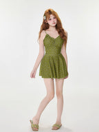 Full body shot of model wearing a green floral print one-piece swimsuit with built-in shorts and sandals.