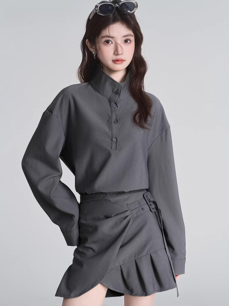 Close-up of a model wearing a grey long-sleeved collared shirt with a high neckline and buttons, paired with a grey skirt.