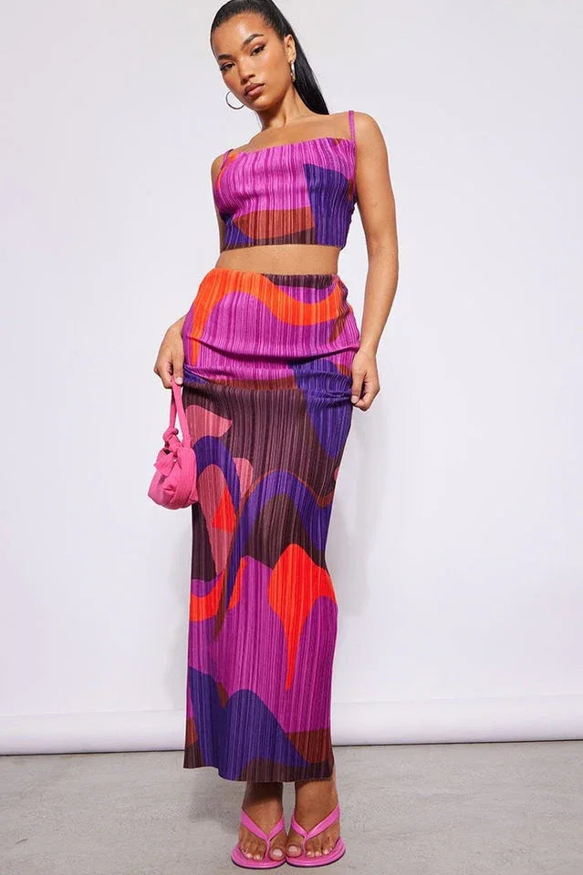 Woman wearing a vibrant abstract print pleated crop top and maxi skirt set with pink accessories. Main image
