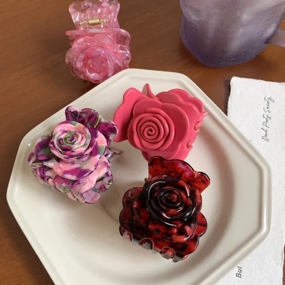 Four rose-shaped hair claw clips in various colors including pink, purple, and red tortoise shell pattern, arranged on a white plate