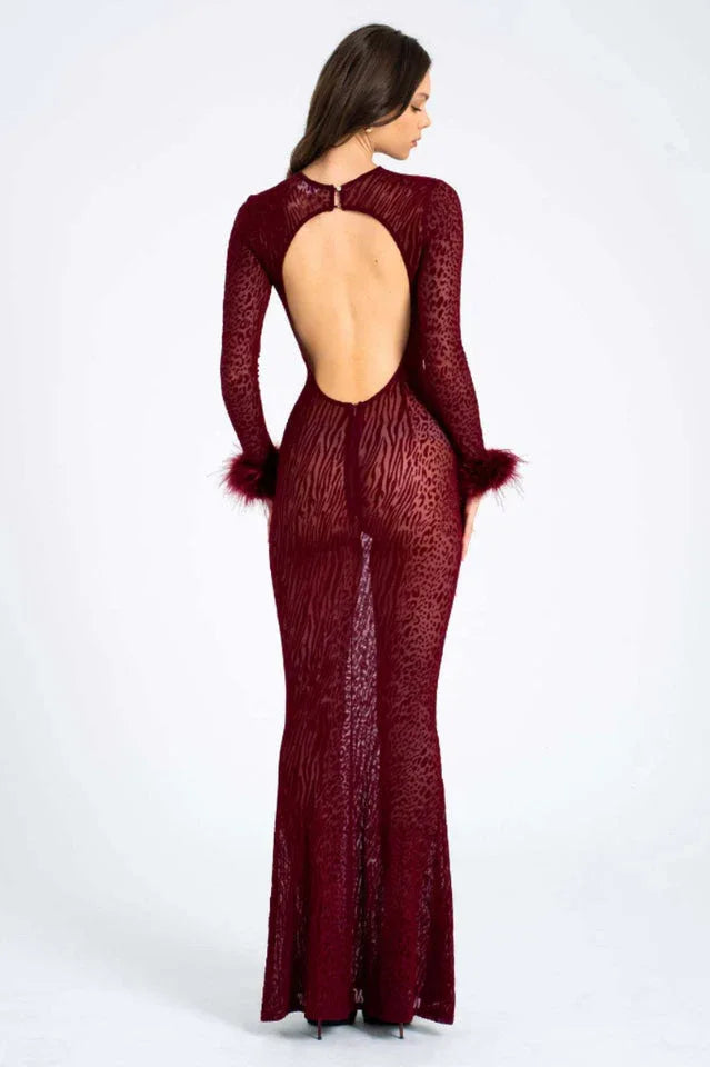 Woman wearing a long-sleeved, burgundy, animal print, sheer mesh dress with feathered cuffs and an open back, back view.