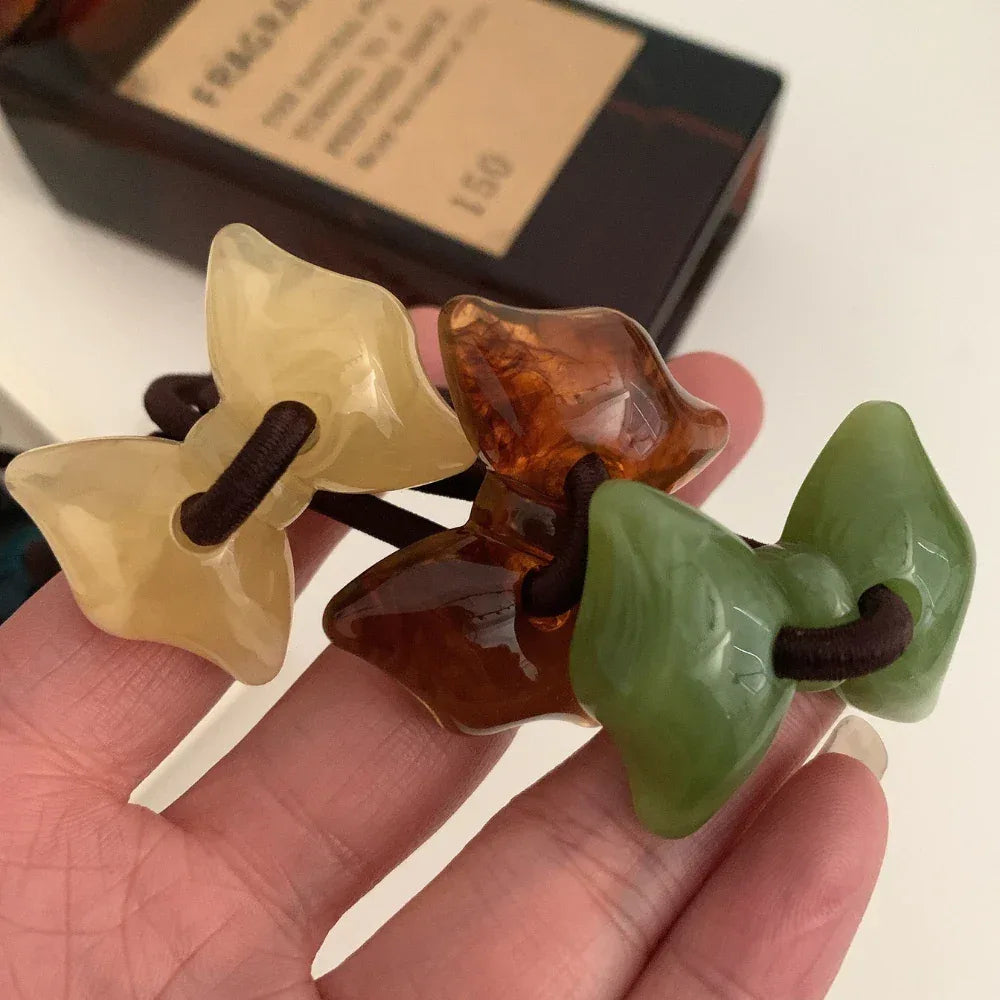 Hand holding yellow, amber, and green bow-shaped hair ties