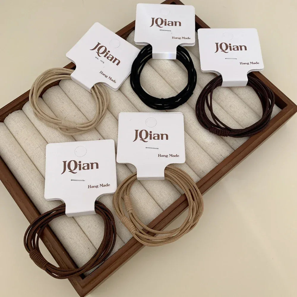 A collection of JQian elastic hair ties in various neutral colors arranged in a wooden tray.