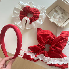 Hand holding a red polka dot headband with scrunchies on a white surface