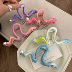 Hand holding a purple S-shaped hair claw clip with a pearl, surrounded by other colorful clips