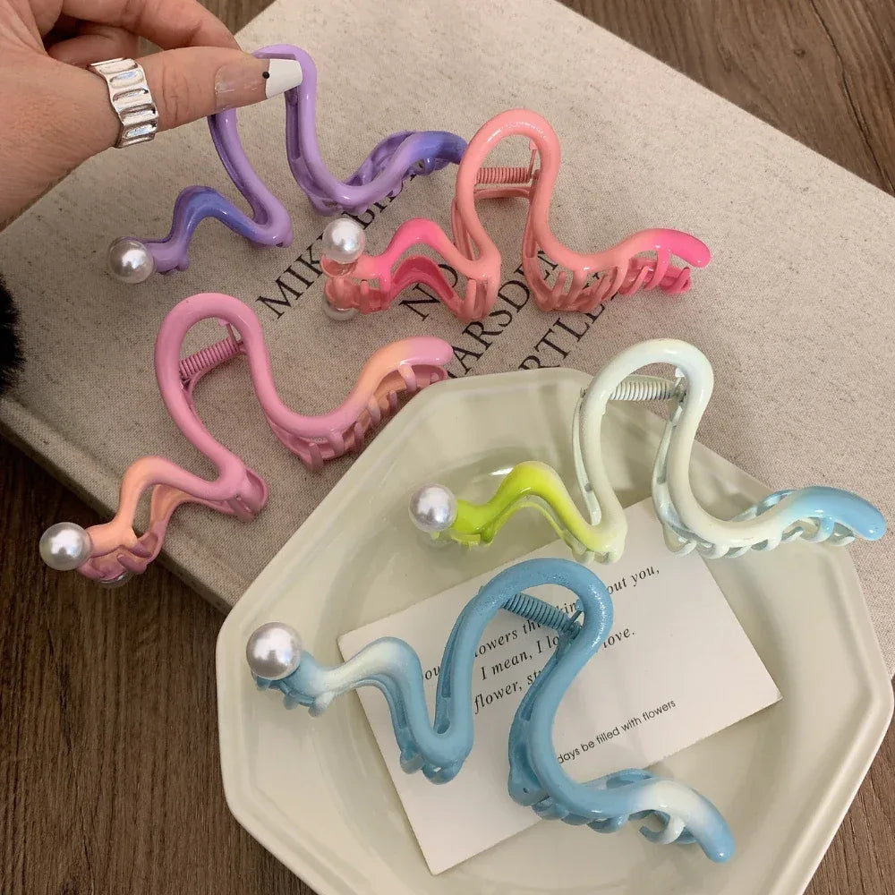 Hand holding a purple S-shaped hair claw clip with a pearl, surrounded by other colorful clips