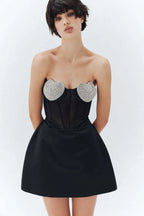 Model wearing a black strapless dress with heart-shaped embellishments on the bust, a corset bodice, and a full skirt, against a white background.