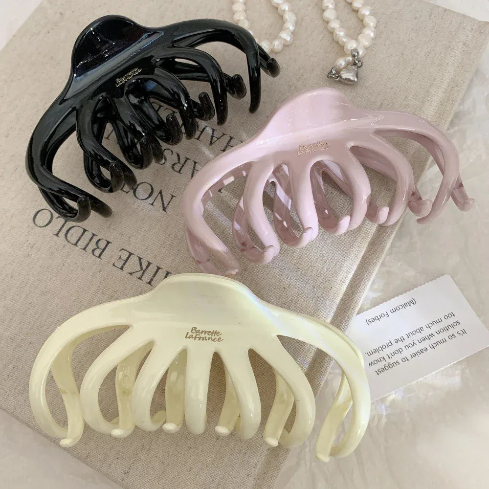 three octopus claw hair clips in black, pink, and cream arranged on a textured surface