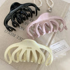 three octopus claw hair clips in black, pink, and cream arranged on a textured surface