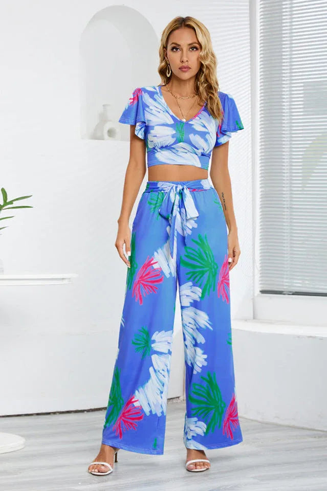 Woman wearing a blue floral print two-piece set with a cropped V-neck top and wide-leg pants, front view.