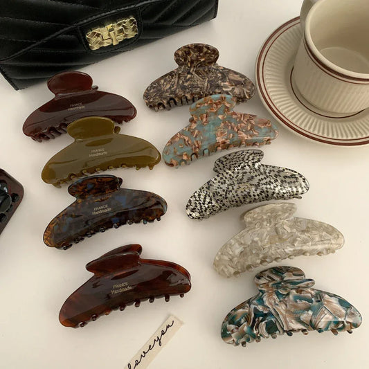 A collection of various tortoiseshell patterned hair claw clips arranged on a white surface, with a black handbag and a coffee cup in the background.
