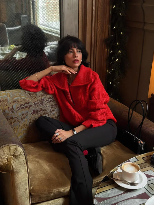 Woman sitting on a couch wearing a red textured knit quarter zip sweater and black pants, with a coffee cup on a table.