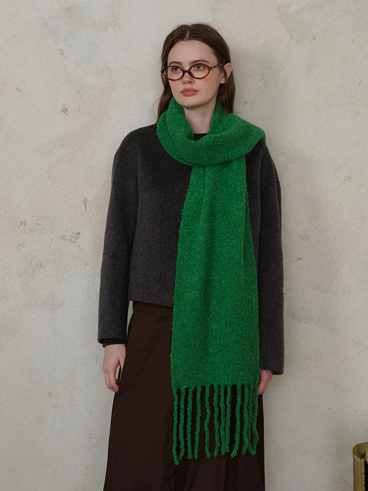 Woman wearing a dark grey sweater and a bright green textured knit scarf with fringe.