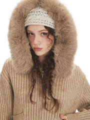 Close-up portrait of a model wearing a beige ribbed knit hooded jacket with faux fur trim, looking at the camera.