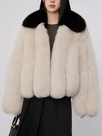 Woman wearing a cream faux fur cropped jacket with a black collar and a black dress, holding a black handbag.