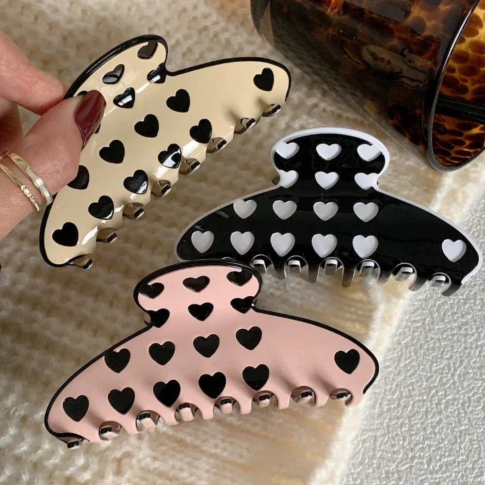 hand holding a beige heart pattern claw clip with other clips nearby