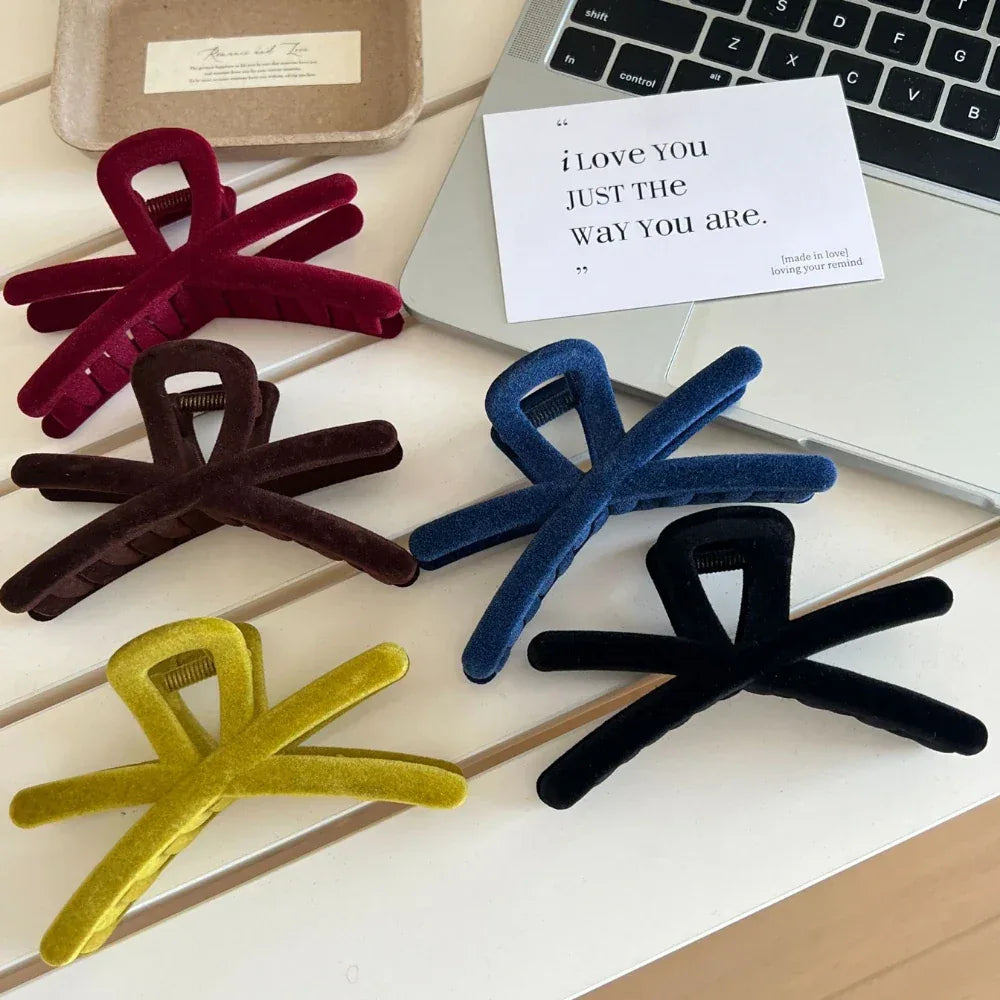 Velvet interlocking hair claw clips in red, brown, blue, black, and yellow, placed near a laptop and a card
